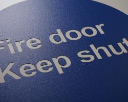 Rotary engraved blue plastic sign with white fire door warning text